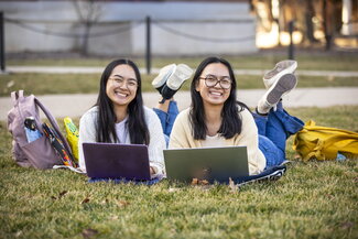 Two students laying on the quad with laptops and smiling.