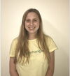 A young woman smiling in a yellow shirt in front of a pale-whiteish background