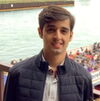 A young man smiling in front of a boat of ppl on a river