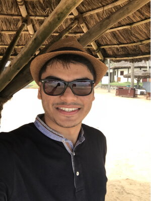 A man in a fedora and black jacket and sunglasses smiling