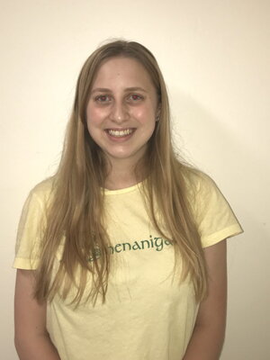 A young woman smiling in a yellow shirt in front of a pale-whiteish background