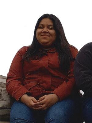 A f\women in a red-brownisg skirt and jeans sitting in a bench