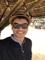 A man in a fedora and black jacket and sunglasses smiling