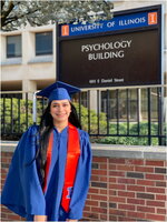 A female in a blue cap and gown in front of the psychology buildingf